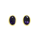 A product photo of a pair of iolite  earrings in 9ct yellow gold sitting on a white background. The fine 6x4mm iolite jewels are framed in a thick layer of yellow gold in a bezel setting. The dark blue colour could make it a good sapphire or tanzanite alternative.