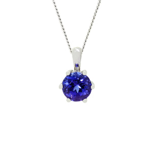 A product photo of a 6mm Round Tanzanite Pendant in 9k White Gold suspended against a white background. The stone is held in place by 6 delicate golden claws. It is suspended by a simple gold chain. The tanzanite reflects violet blue hues across its multi-faceted edges.