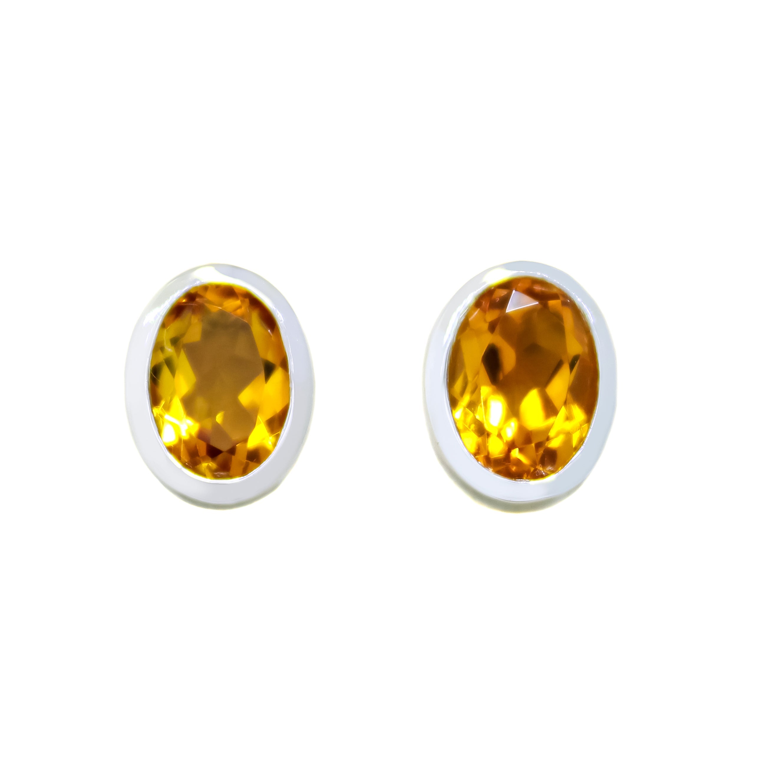 A product photo of a pair of citrine earrings in 9ct white gold sitting on a white background. The fine 7x5mm citrines are framed in a thick layer of white gold in a bezel setting.