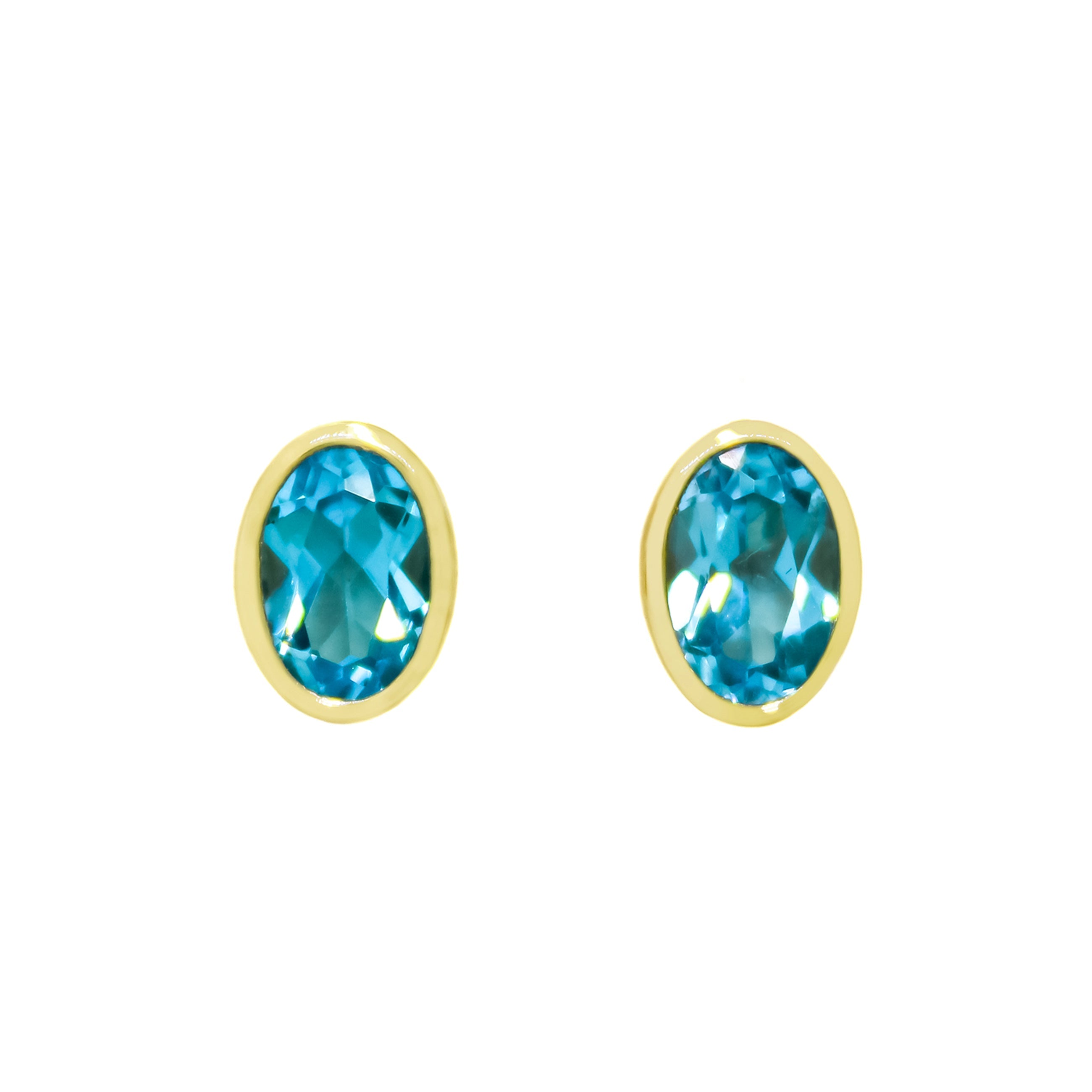 A product photo of a pair of blue topaz gold earrings sitting on a white background. The fine 6x4mm topaz stones are framed in a thick layer of yellow gold in a bezel setting.