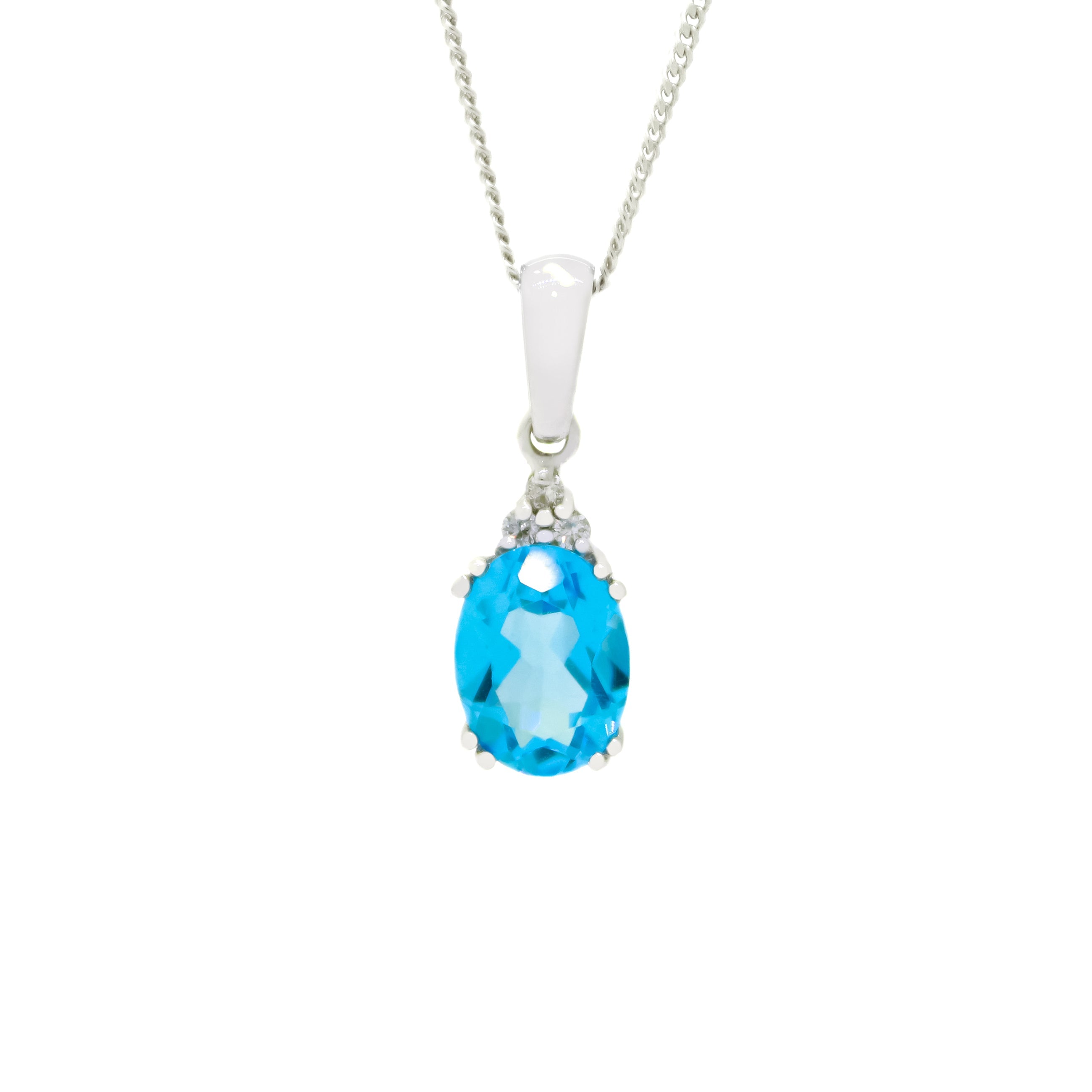 A product photo of a white gold blue topaz necklace sitting against a white background. The light blue oval-cut stone is held in place by 4 pairs of claws at its top and bottom, with a trio of white diamonds connecting the stone to the rest of the pendant. It is suspended by a simple white gold chain.