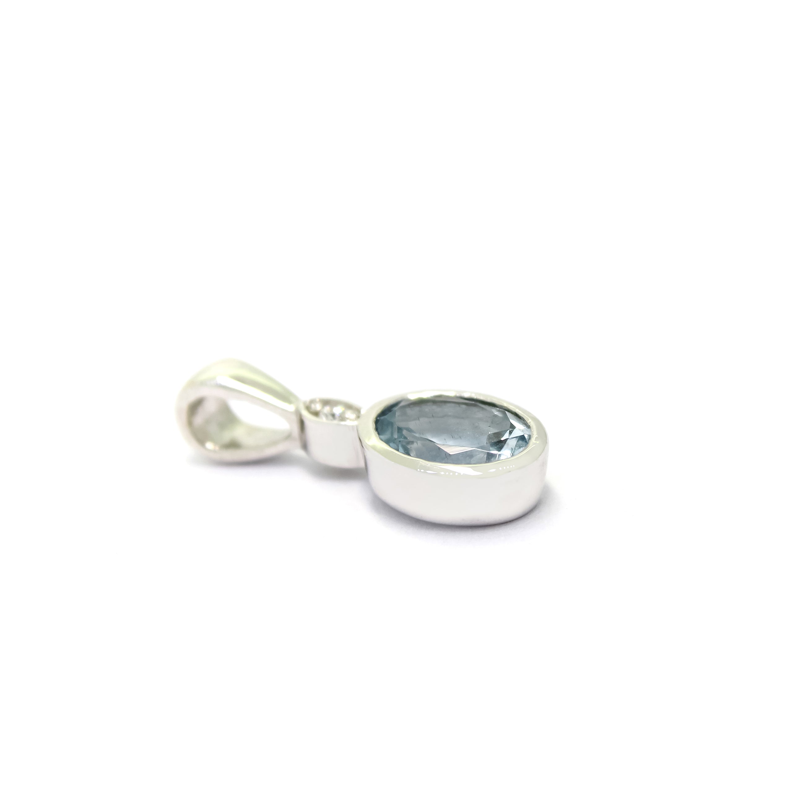 A product photo of a Bezel-set Aquamarine Pendant and diamond in 9ct White Gold suspended by a gold chain on a plain white background. Above the bezel-set aquamarine stone sits a single white diamond, also encased in white gold.