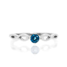 A product photo of an ornate silver ring with a london blue topaz centre stone sitting on a white background. The silver band splits halfway along its length, becoming twisting and serpentine in appearance before meeting on either side of the dazzling blue 3.5mm stone, which is held in place by 4 silver claws.