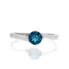 A product photo of a curved-band silver solitaire ring with an ocean blue London Blue Topaz centre stone sitting on a white background. The deep blue gemstone colour be a good sapphire substitute.