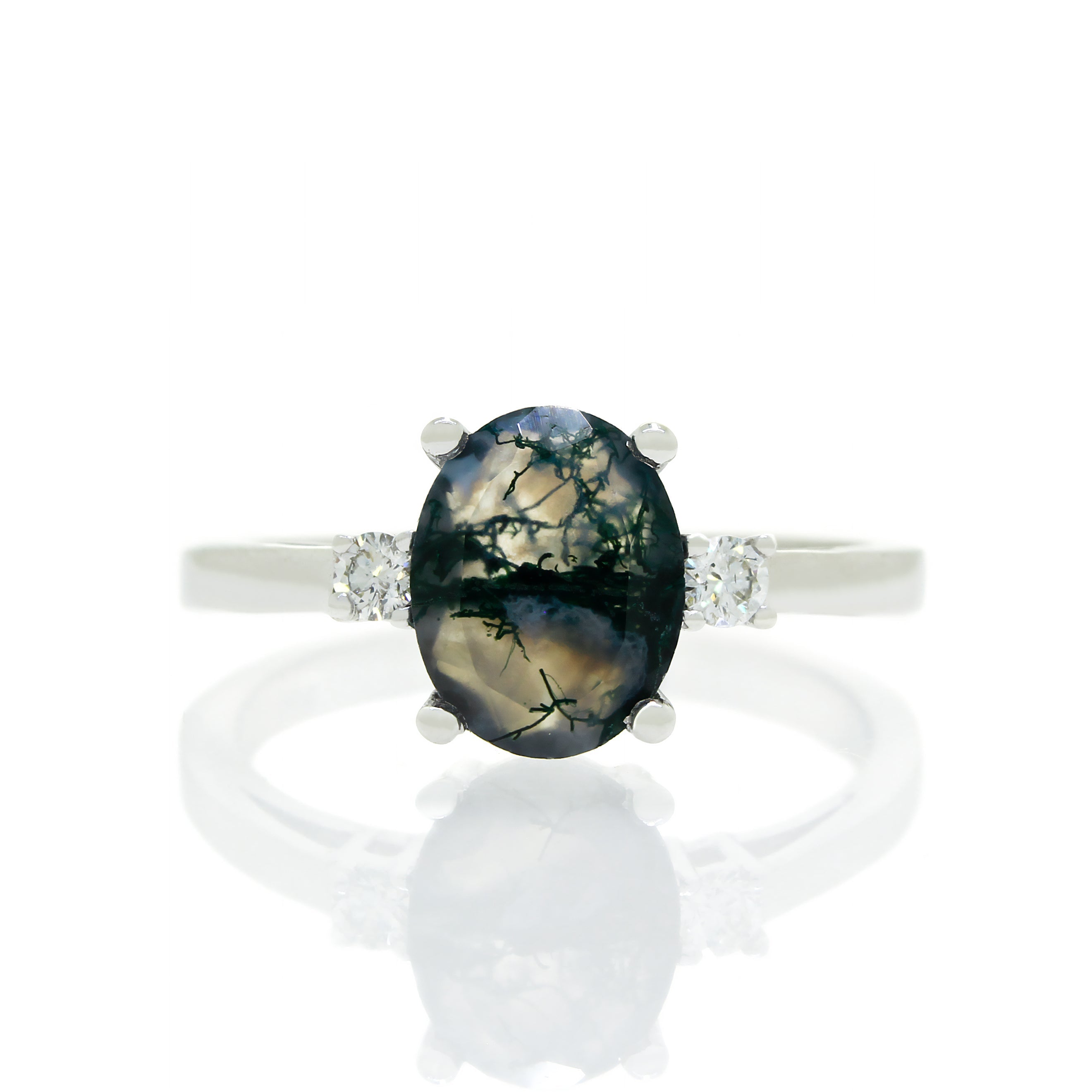 A product photo of a dainty and elegant white gold ring with a stunning trio of moss agate and diamonds sitting against a white background. The large centre stone is hugged by two smaller circular white diamonds on either side.