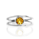 A product photo of a split-band silver ring with a bezel-set citrine centre stone sitting on a white background. The silver band splits at the base of the ring, separating to meet at the top and bottom of the bright orange round-cut centre stone, framed in a thick layer of silver, holding it in place.