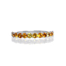 A product photo of a silver eternity band with 13 citrine stones embedded along its length on a white background.