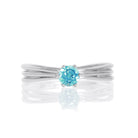 A product photo of a simple silver solitaire ring with a unique band detail and a 4mm round blue topaz centre stone sitting on a white background. The band is styled to appear as 3 little silver bands, tilted slightly outwards and "overlapping" towards the back of the ring.