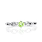 A product photo of an ornate silver ring with a peridot centre stone sitting on a white background. The silver band splits halfway along its length, becoming twisting and serpentine in appearance before meeting on either side of the dazzling green 3.5mm stone, which is held in place by 4 silver claws.