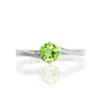 A product photo of a curved-band silver solitaire ring with a grass green peridot centre stone sitting on a white background.