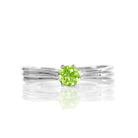 A product photo of a simple silver solitaire ring with a unique band detail and a 4mm round peridot centre stone sitting on a white background. The band is styled to appear as 3 little silver bands, tilted slightly outwards and "overlapping" towards the back of the ring.