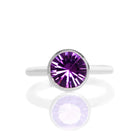 A product photo of a silver ring with a bezel-set amethyst centre stone sitting on a white background. The silver band is simple and smooth, connecting on either side of a large, statement-sized garnet stone surrounded by a solid frame of silver.