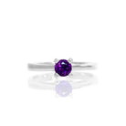 A product photo of a silver solitaire ring with an amethyst centre stone sitting on a white background. The silver band is simple and smooth, and the amethyst stone is held in place by 4 delicate silver claws.