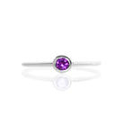 A product photo of a delicate silver stacking ring with a tiny, bezel-set amethyst in the centre sitting on a white background. The band is slim and thread-like, with the focus drawn to the petite 3mm glinting purple centre stone.