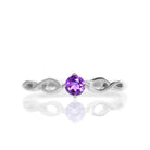 A product photo of an ornate silver ring with an amethyst centre stone sitting on a white background. The silver band splits halfway along its length, becoming twisting and serpentine in appearance before meeting on either side of the dazzling purple 3.5mm stone, which is held in place by 4 silver claws.