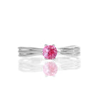 A product photo of a simple silver solitaire ring with a unique band detail and a 4mm round pink tourmaline centre stone sitting on a white background. The band is styled to appear as 3 little silver bands, tilted slightly outwards and "overlapping" towards the back of the ring.