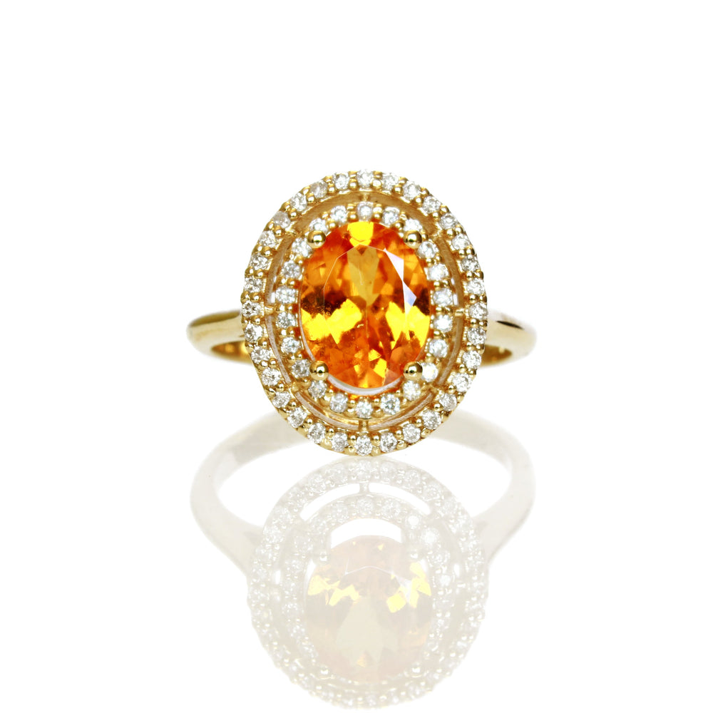 A product photo of an elaborate orange mandarin garnet and diamond engagement ring in solid 14 karat yellow gold on a white background. The ring is composed of a large electric orange garnet stone, surrounded by a double halo of diamonds (54 total) and held in place by ornate golden detailing.