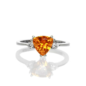 A product photo of an orange mandarin garnet solitaire ring in solid 9 karat white gold on a white background. The ring is composed of a simple rounded gold band, a 7mm bright orange trilliant garnet stone in the cente, and one 0.06ct diamond on either side.