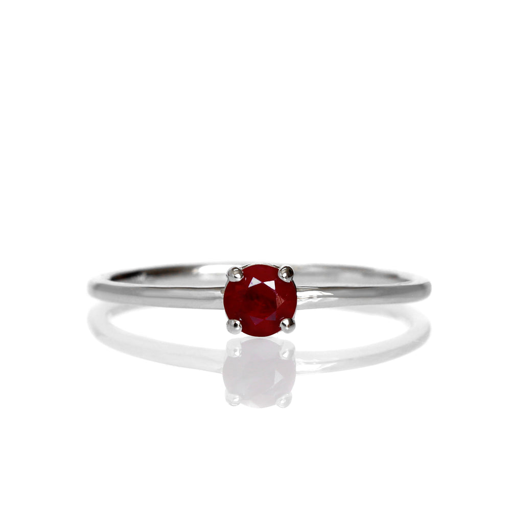 A product photo of a delicate white gold stacking ring with a tiny, claw-set ruby in the centre sitting on a white background. The band is slim and thread-like, with the focus drawn to the petite 4mm glinting burgundy red gemstone.