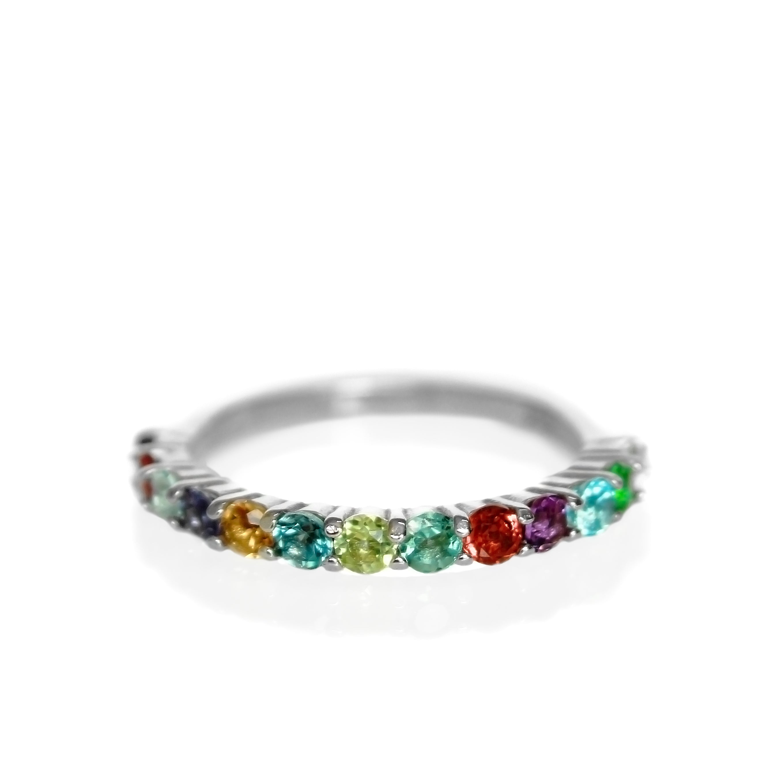 A silver multi-gemstone eternity ring sitting on a white reflective background. The ring is made up of 13 2.5mm round-cut semi-precious gemstones in a rainbow of colours.