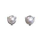 A product photo of a pair of white pearl and diamond stud earrings on a white background. The pearls are 7mm wide and perfectly round, and are set within swirling frames of solid white gold, featuring three tiny diamonds on each earring.