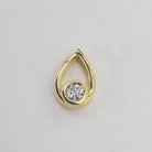 A product photo of a moissanite pendant in yellow gold sits on a clear white background. The pendant is in the shape of a small teardrop, with a petite gold-encased circle-cut moissanite gem nestled at its base. The yellow gold teardrop is smooth and unblemished. 